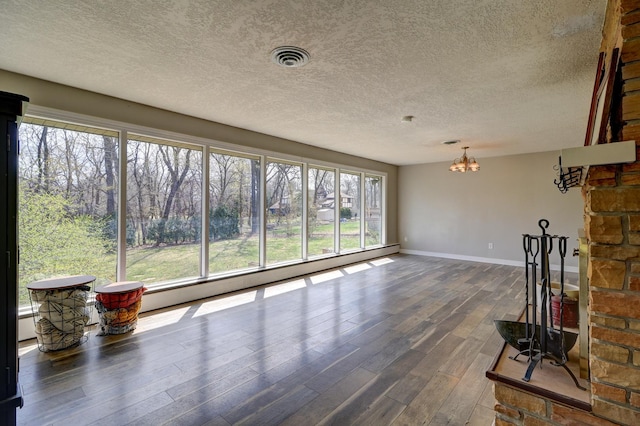 unfurnished living room with a chandelier, dark wood-type flooring, baseboards, a baseboard radiator, and a textured ceiling