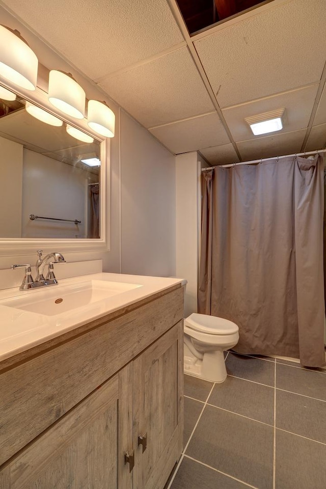 full bathroom featuring tile patterned floors, vanity, a drop ceiling, a shower with curtain, and toilet