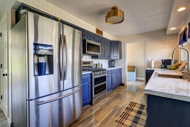 kitchen with a textured ceiling, a sink, stainless steel appliances, blue cabinetry, and visible vents
