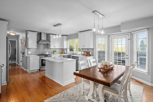 kitchen featuring wall chimney range hood, backsplash, appliances with stainless steel finishes, and light countertops