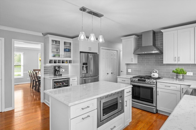 kitchen featuring crown molding, decorative backsplash, wall chimney exhaust hood, white cabinets, and stainless steel appliances