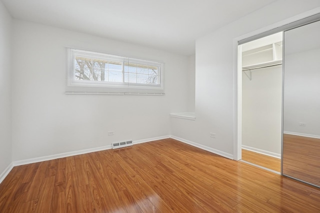 unfurnished bedroom featuring baseboards, wood finished floors, visible vents, and a closet