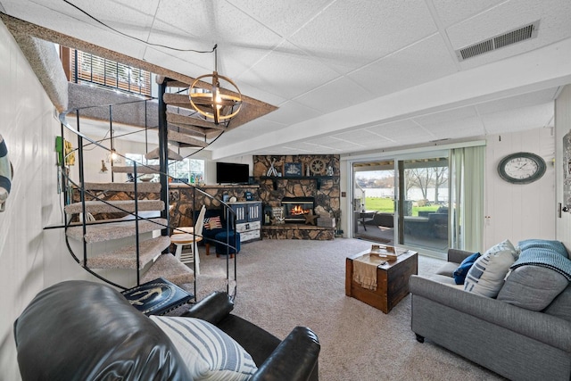 carpeted living room with a stone fireplace, visible vents, and stairs