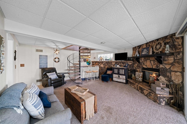 carpeted living area with a stone fireplace, visible vents, and a drop ceiling