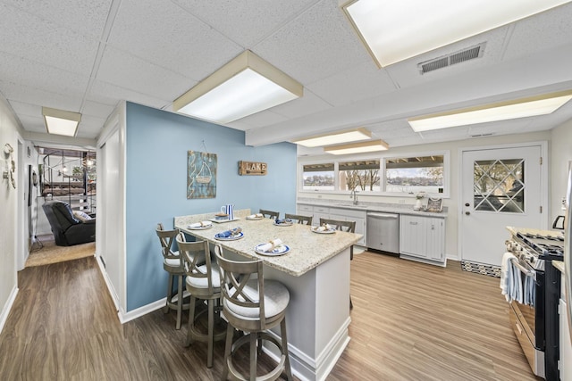 kitchen with a sink, baseboards, light wood-style floors, appliances with stainless steel finishes, and a breakfast bar area