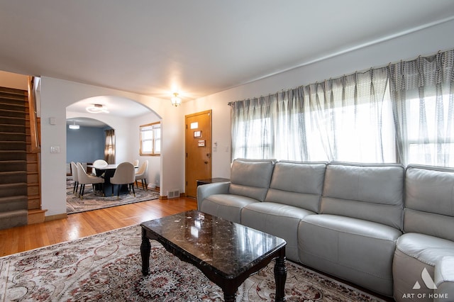 living area with light wood-type flooring, baseboards, stairway, visible vents, and arched walkways