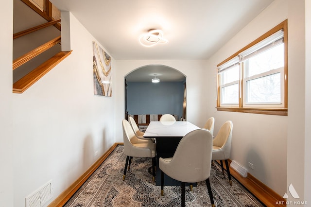 dining space featuring arched walkways, visible vents, baseboards, and wood finished floors