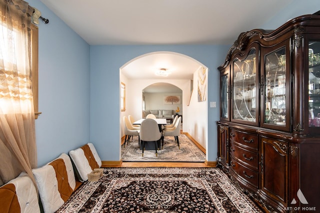 dining room featuring arched walkways, wood finished floors, and baseboards