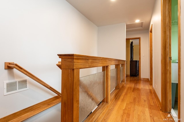 hall with attic access, light wood finished floors, visible vents, and an upstairs landing