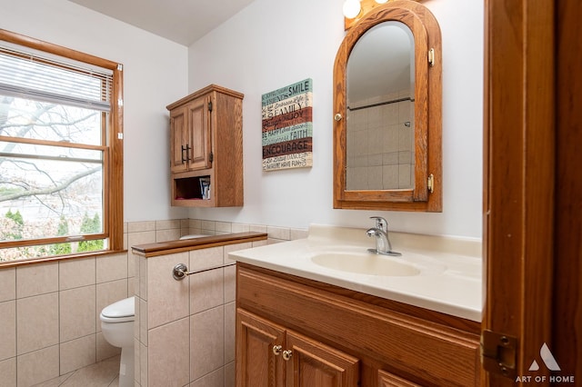 bathroom featuring toilet, a healthy amount of sunlight, wainscoting, and tile walls