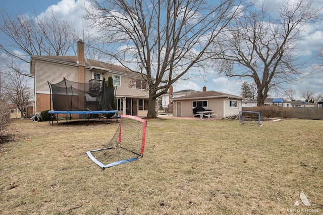 back of property featuring an outdoor structure, a lawn, a chimney, fence, and a trampoline
