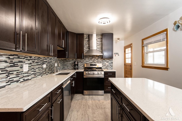 kitchen with light stone countertops, wall chimney range hood, a sink, stainless steel appliances, and backsplash