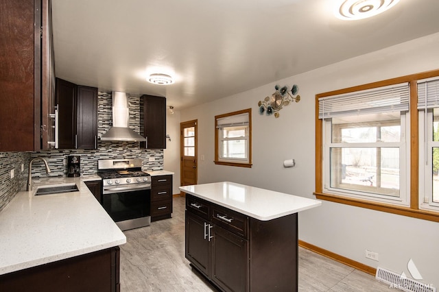 kitchen featuring tasteful backsplash, stainless steel range with gas stovetop, wall chimney exhaust hood, a sink, and a healthy amount of sunlight