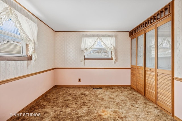 carpeted spare room featuring wallpapered walls, baseboards, visible vents, and crown molding