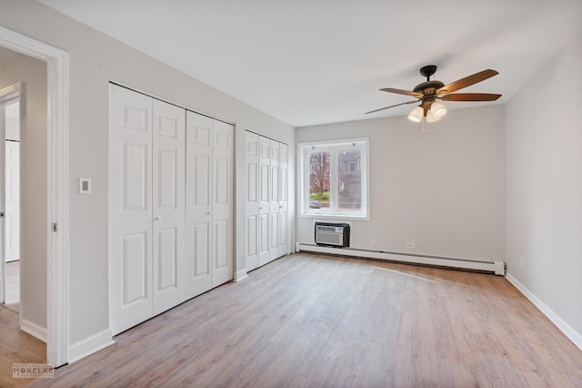 unfurnished bedroom with baseboards, wood finished floors, two closets, a wall mounted AC, and a baseboard radiator