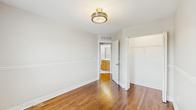 unfurnished bedroom with baseboards, visible vents, wood finished floors, and a closet