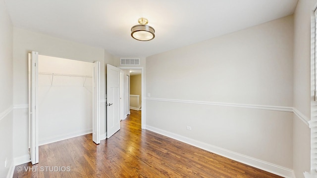 unfurnished bedroom with baseboards, visible vents, wood finished floors, and a closet