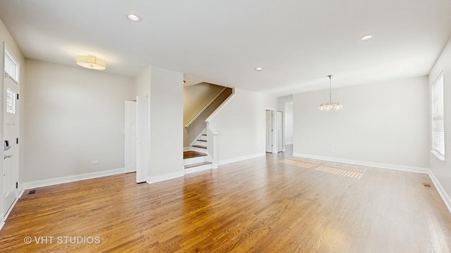 unfurnished living room featuring light wood-style floors, baseboards, stairs, and a notable chandelier