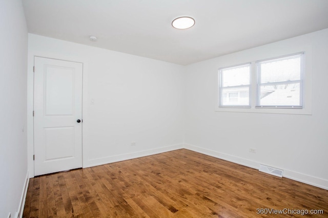 spare room with baseboards, wood finished floors, and visible vents
