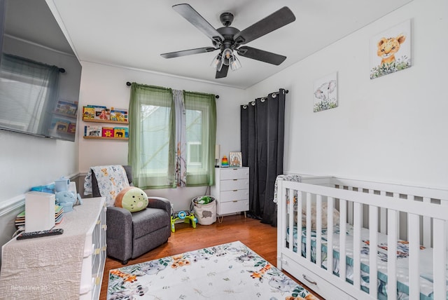 bedroom with a nursery area, ceiling fan, and wood finished floors