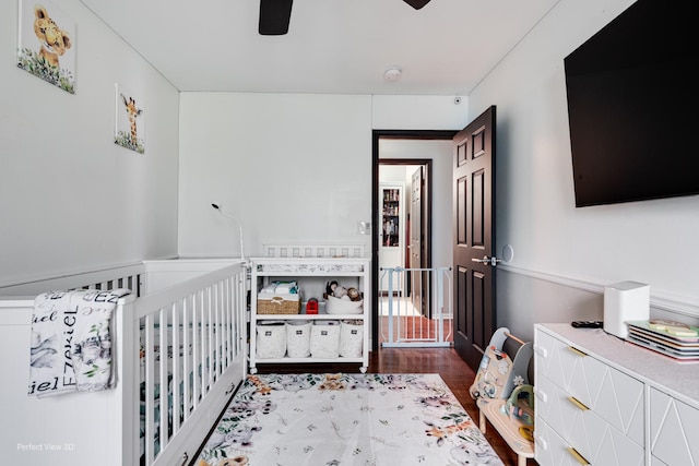 bedroom with a nursery area, wood finished floors, and ceiling fan