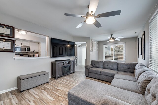 living area with light wood-style floors, baseboards, and ceiling fan