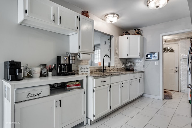 kitchen with marble finish floor, decorative backsplash, a sink, and white cabinets