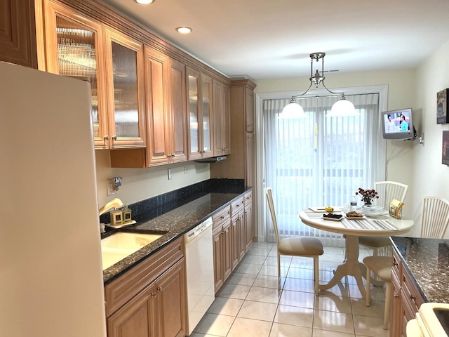 kitchen with dark stone countertops, white dishwasher, a sink, light tile patterned floors, and freestanding refrigerator