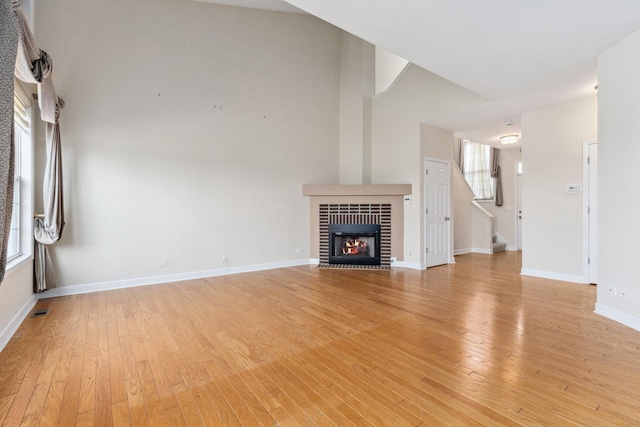 unfurnished living room featuring visible vents, baseboards, a fireplace, stairs, and light wood-style flooring