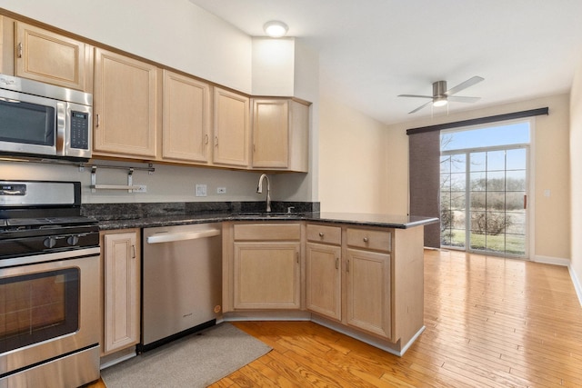 kitchen featuring a sink, light wood-type flooring, appliances with stainless steel finishes, a peninsula, and light brown cabinetry