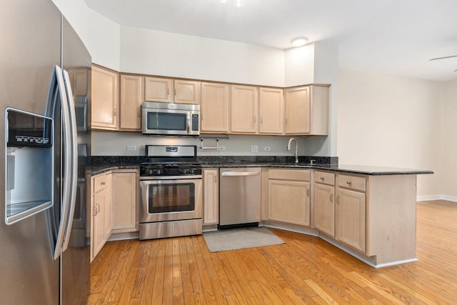 kitchen with light wood-style flooring, a peninsula, a sink, stainless steel appliances, and light brown cabinets