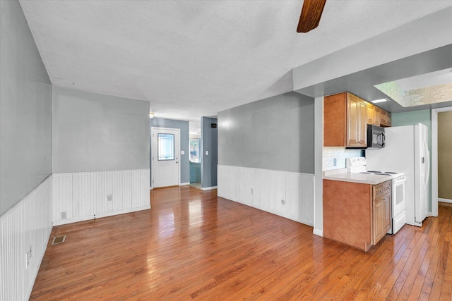 2240 Marilyn Dr, Saint Joseph, IL 61873 - kitchen featuring electric stove, black microwave, light wood-style flooring, a wainscoted wall, and a textured ceiling