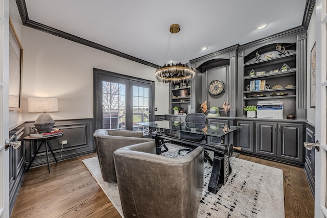 office featuring a decorative wall, wood finished floors, built in shelves, a wainscoted wall, and ornamental molding