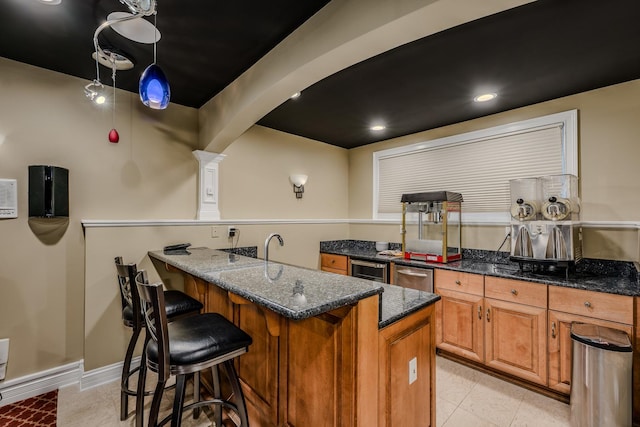 kitchen with brown cabinetry, a peninsula, dark stone counters, and a breakfast bar