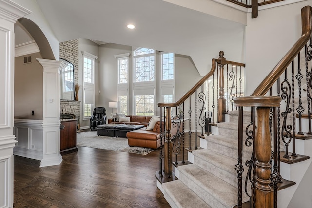 stairway featuring a high ceiling, wood finished floors, visible vents, arched walkways, and a fireplace