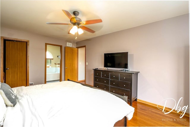 bedroom featuring visible vents, wood finished floors, baseboards, ceiling fan, and ensuite bath