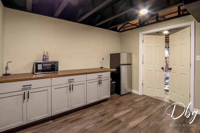 kitchen with black microwave, dark wood finished floors, baseboards, freestanding refrigerator, and butcher block counters