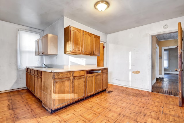 kitchen featuring light wood-style flooring, a sink, baseboards, brown cabinets, and light countertops