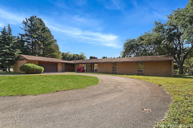 ranch-style home featuring a front yard, brick siding, curved driveway, and a garage