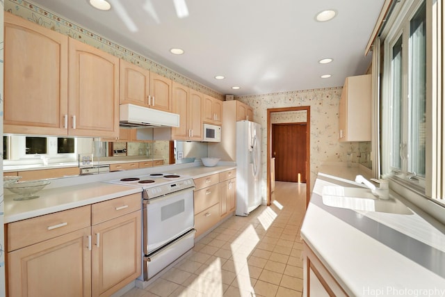 kitchen featuring under cabinet range hood, light brown cabinetry, white appliances, and a sink