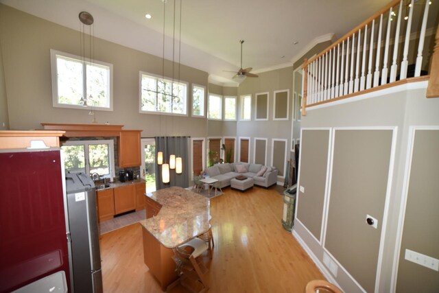 kitchen featuring stainless steel refrigerator with ice dispenser, ceiling fan, a high ceiling, open floor plan, and light wood-style floors