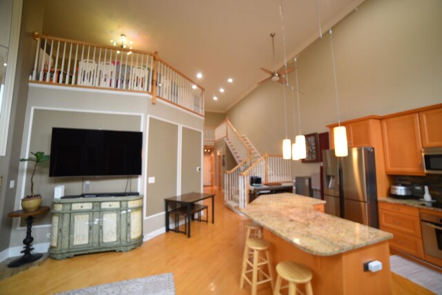 kitchen featuring a high ceiling, a ceiling fan, a glass covered fireplace, open floor plan, and light wood-type flooring