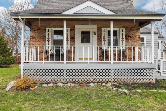 back of property with covered porch, brick siding, a yard, and roof with shingles