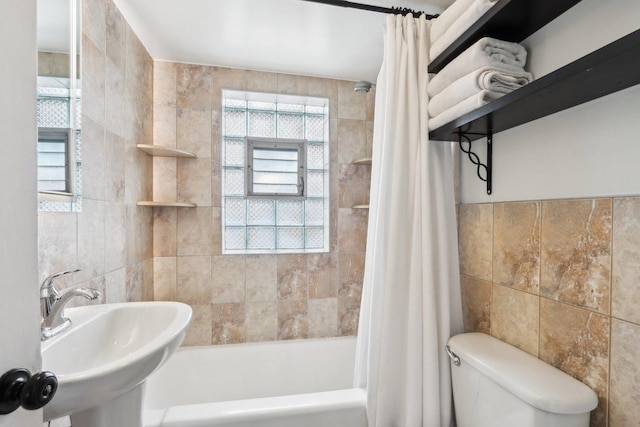 bathroom with tile walls, shower / bathtub combination with curtain, toilet, and a sink