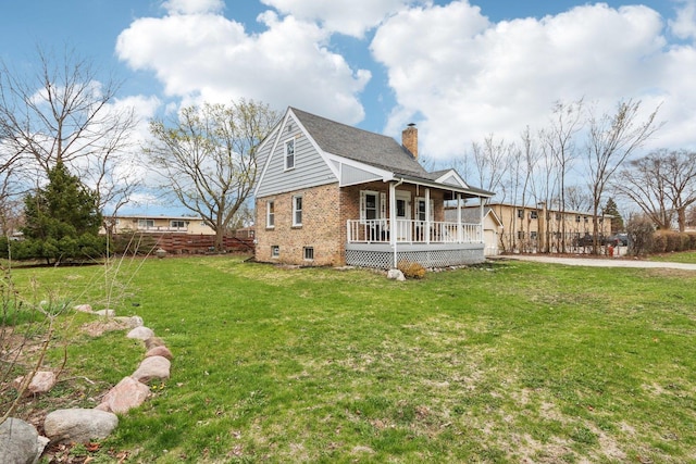 view of side of home with a chimney, brick siding, a porch, and a yard