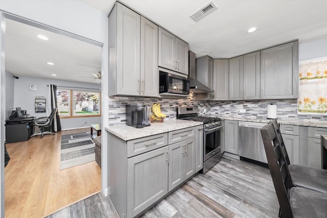 kitchen with stainless steel appliances, gray cabinetry, wall chimney range hood, backsplash, and recessed lighting