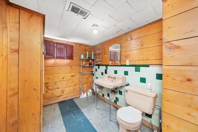 bathroom with toilet, tile patterned floors, wood walls, and a sink