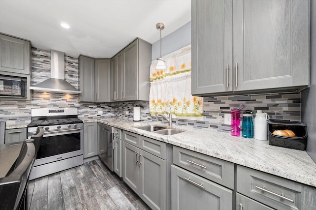 kitchen featuring gray cabinetry, stainless steel appliances, wall chimney exhaust hood, a sink, and dark wood-style flooring