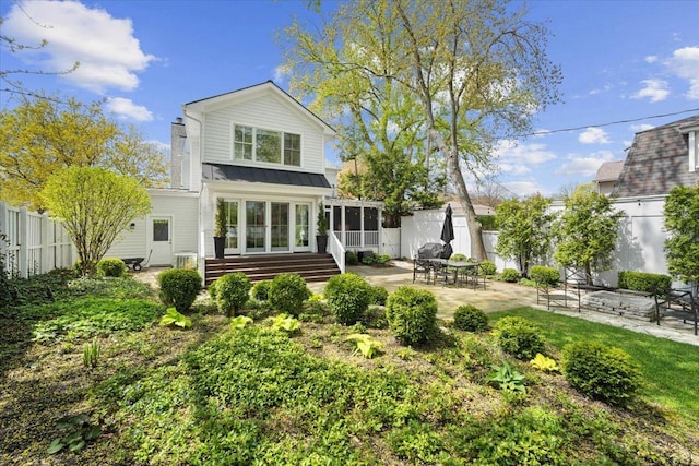 back of house with a standing seam roof, metal roof, a patio area, a sunroom, and fence