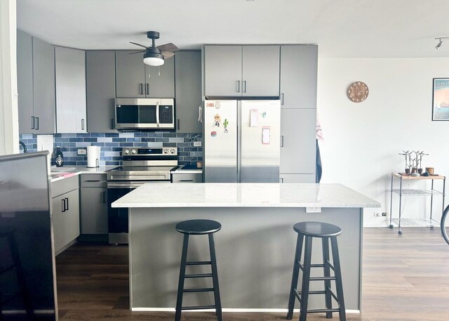 kitchen featuring gray cabinetry, dark wood-style flooring, appliances with stainless steel finishes, and a kitchen bar